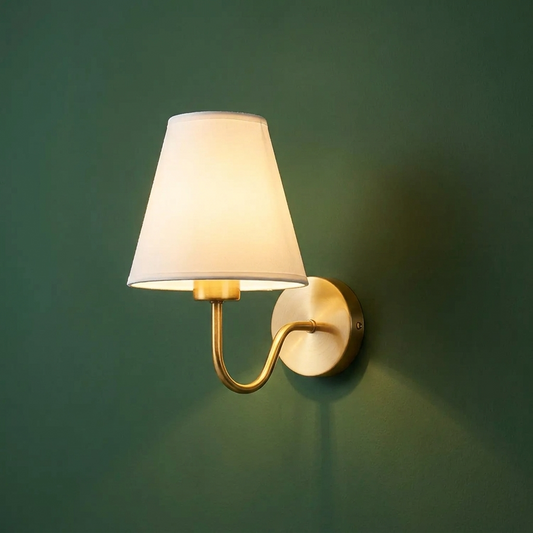 Gold iron wall sconce with a white fabric shade facing up, mounted on a deep green wall